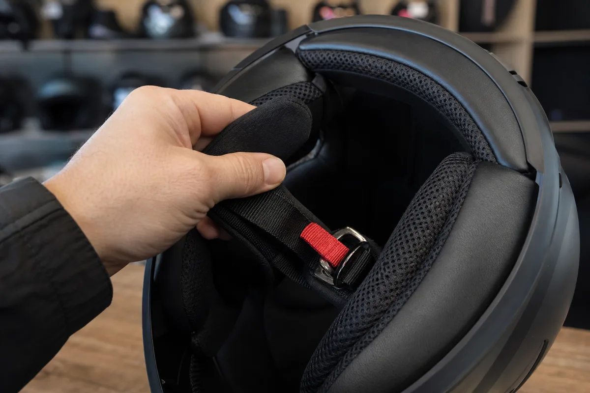 Main soulevant la jugulaire intérieure d&rsquo;un casque moto ouvert dans une boutique d&rsquo;équipement