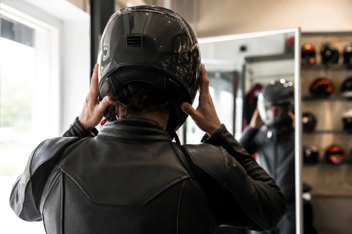 Personne vue de dos ajustant un casque moto devant un miroir de boutique