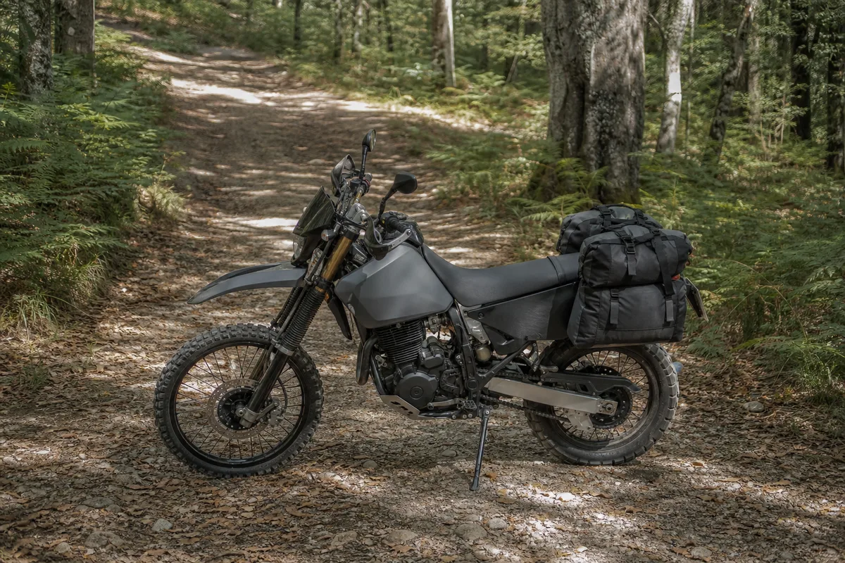 Trail léger garé sur un chemin de terre en bord de forêt, roue avant à rayons et bagagerie souple