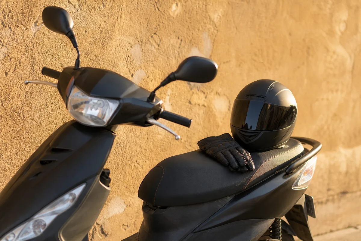 Scooter cinquante centimètres cubes garé devant un mur crépi ocre, casque posé sur la selle