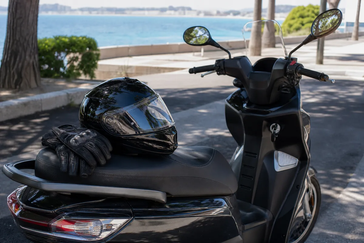 Casque intégral et gants de moto posés sur la selle d&rsquo;un scooter 125 garé à l&rsquo;ombre